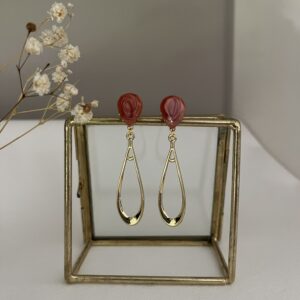 Lange slanke oorbellen van metaal aan een donkerrode RVS oorsteker