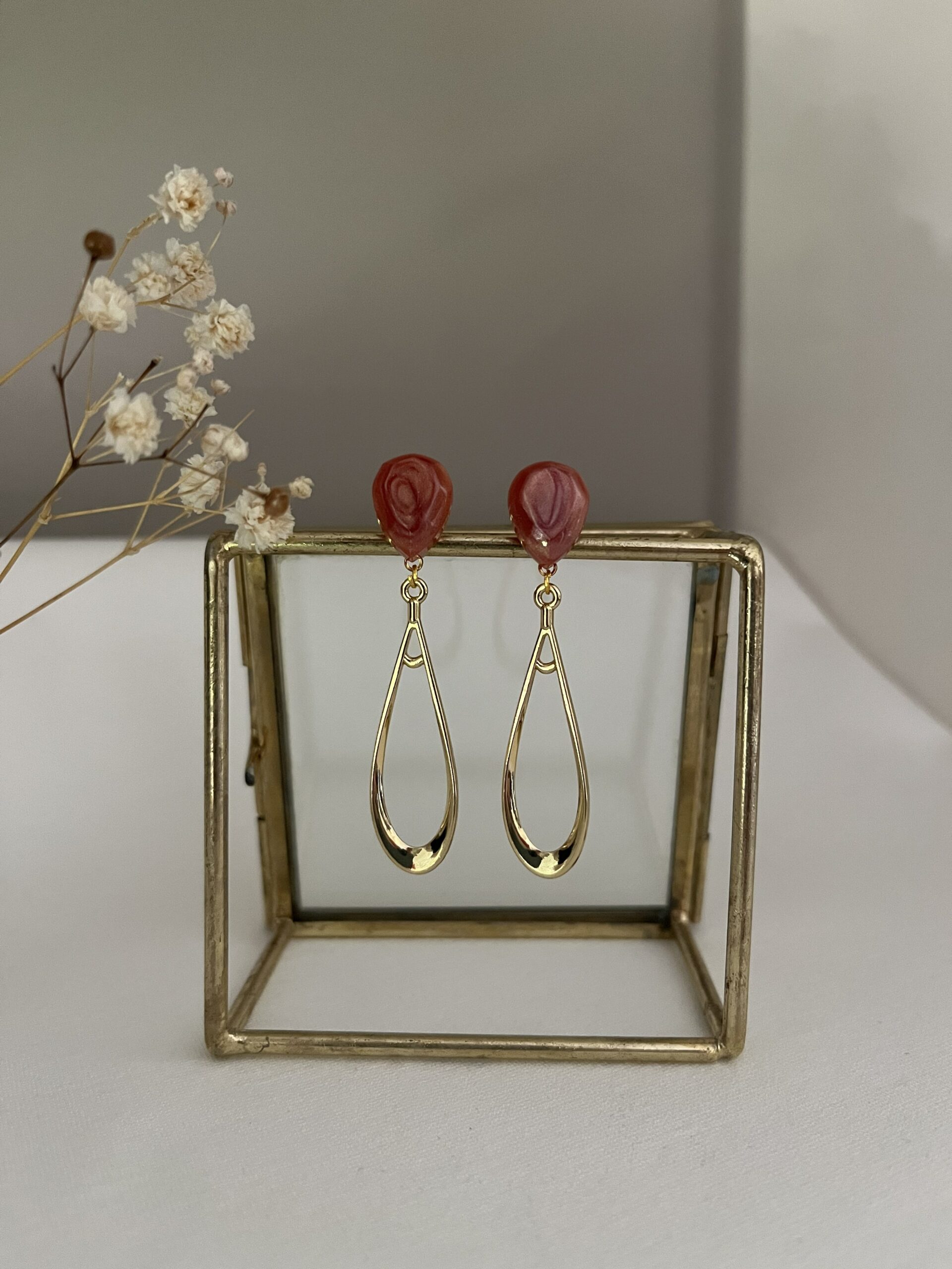 Lange slanke oorbellen van metaal aan een donkerrode RVS oorsteker