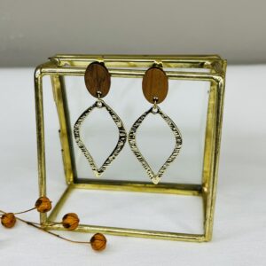 Opvallende oorbellen van goudkleurig bewerkt metaal in druppelvorm aan een houten oorsteker